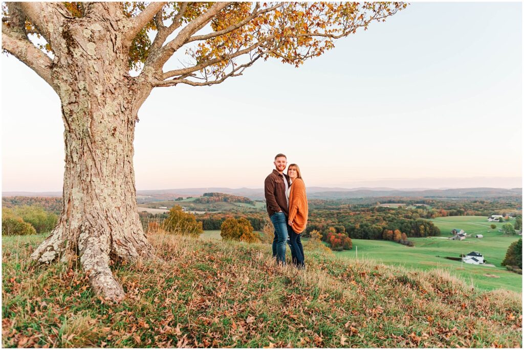 engagement couple standing on a hill next to a tree in West Virginia