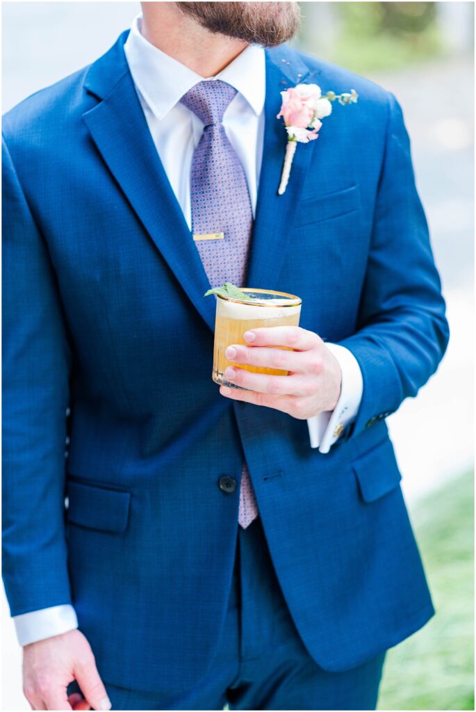 the groom holding an orange drink in a clear and gold rimmed glass during cocktail hour 