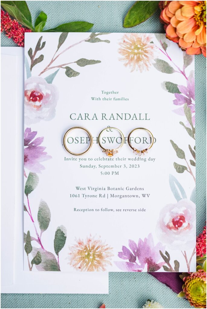 three wedding rings sitting on an invitation surrounded by bright flowers 