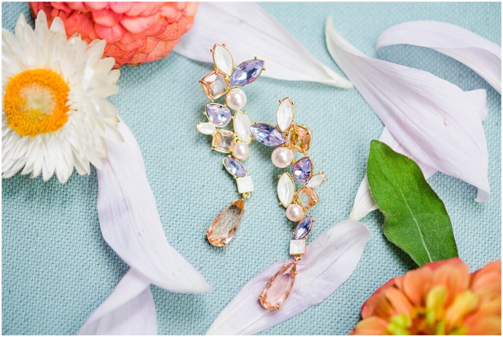 peach, purple, and pearl dangly earrings sitting on a blue mat next to bright flowers 