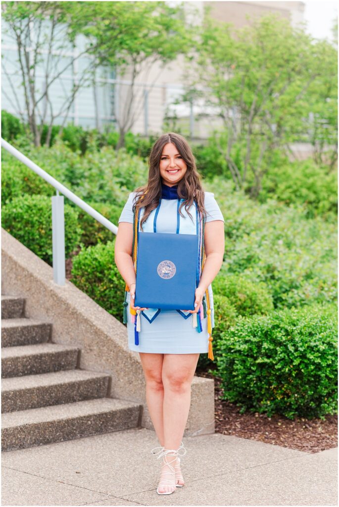 graduate student posing on the stairs with her diploma at the West Virginia College of Law building