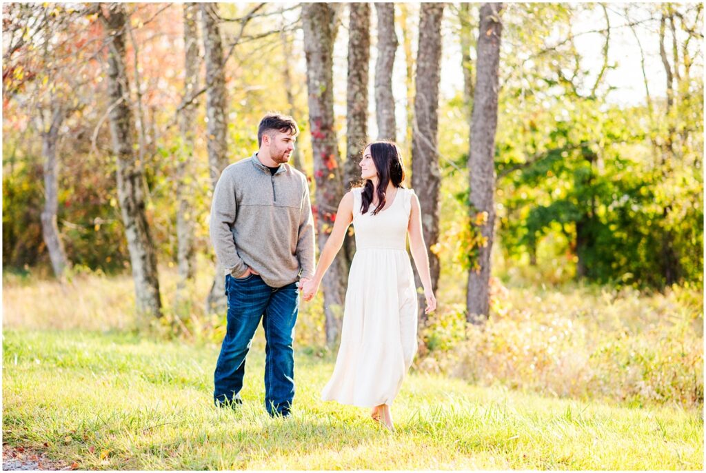 couple walking hand in hand next to a field and trees in Morgantown, WV