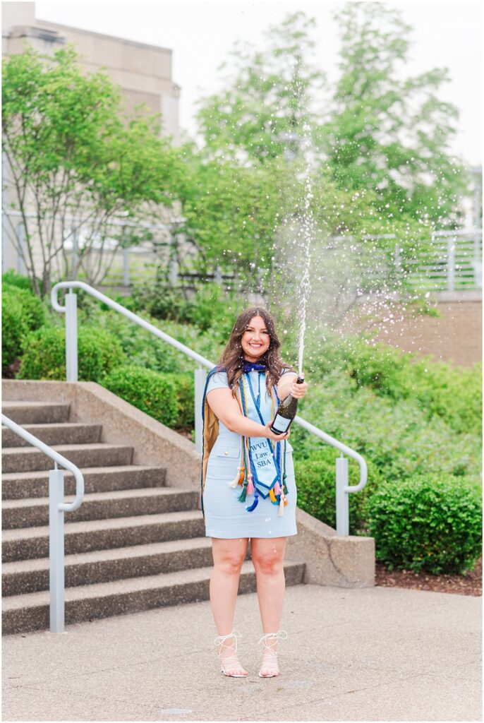 law school graduate spraying a bottle of prosecco at the bottom of the stairs at WVU