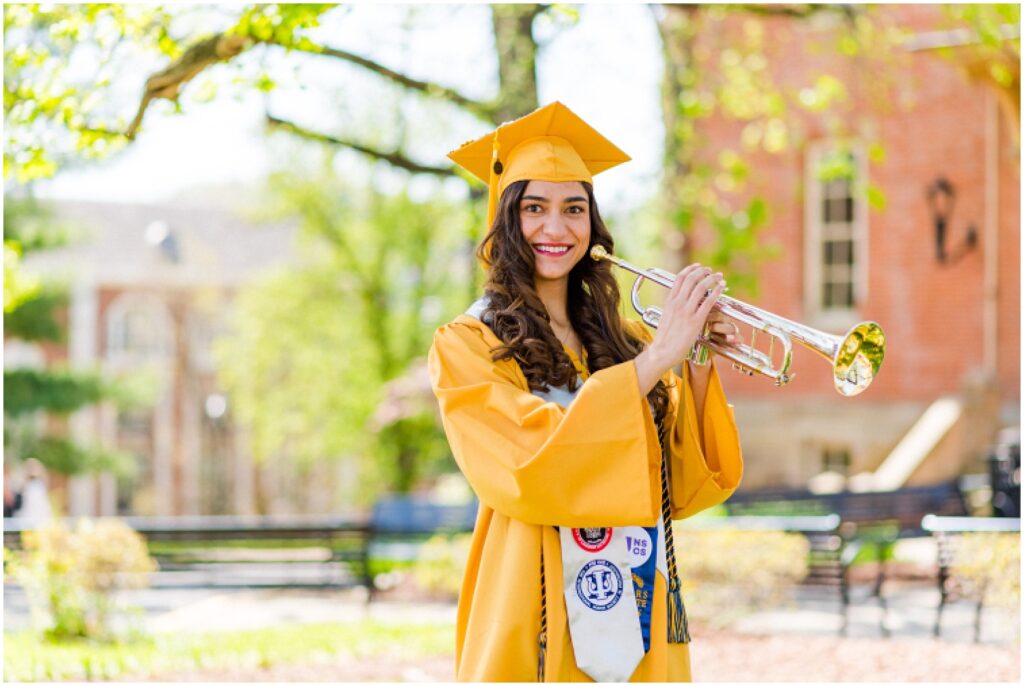 WVU college student wearing a yellow cap and gown holding her trumpet
