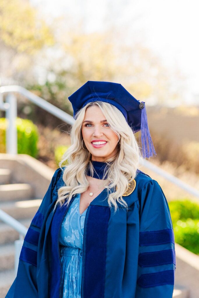 woman in a blue graduation gown and cap with tassel smiling outdoors on steps