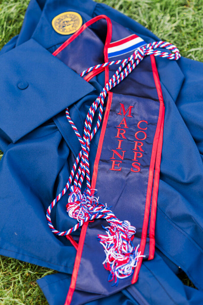 blue graduation gown with red white and blue cords and a marine corps stole laid on grass