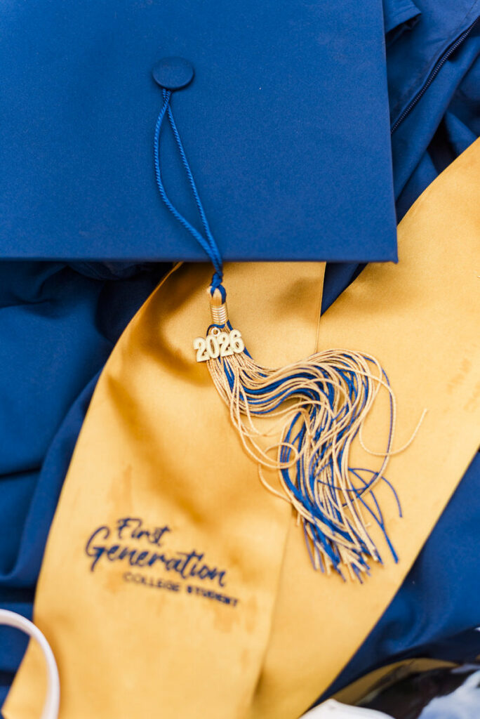 wvugradphotos270 carrie white photography blue graduation cap with a gold tassel marked resting on a yellow stole that reads'First Generation College Student'.