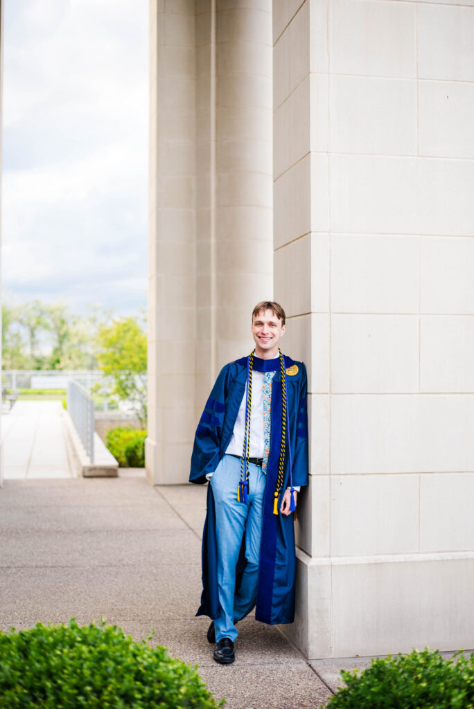 graduationphotoideasfor guys066 carrie white photography graduation photo ideas for guys show law graduate in blue cap and gown standing beside a stone column on a campus pathway smiling at the camera
