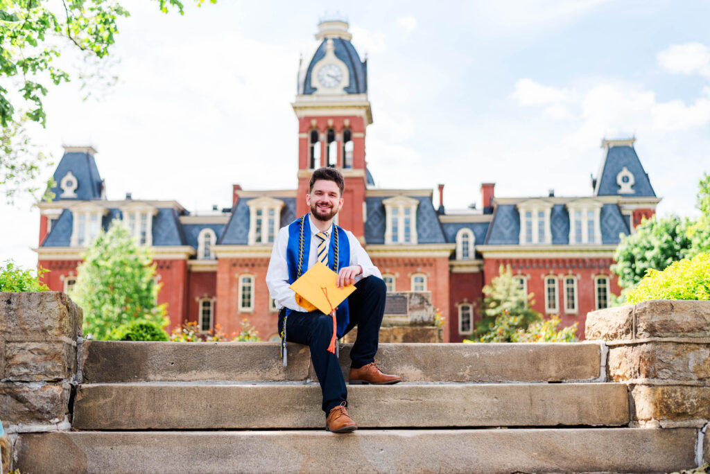 graduationphotoideasfor guys145 carrie white photography graduate in blue stole posing on campus steps with a yellow envelope clocktower building in the background for graduation photo ideas for guys