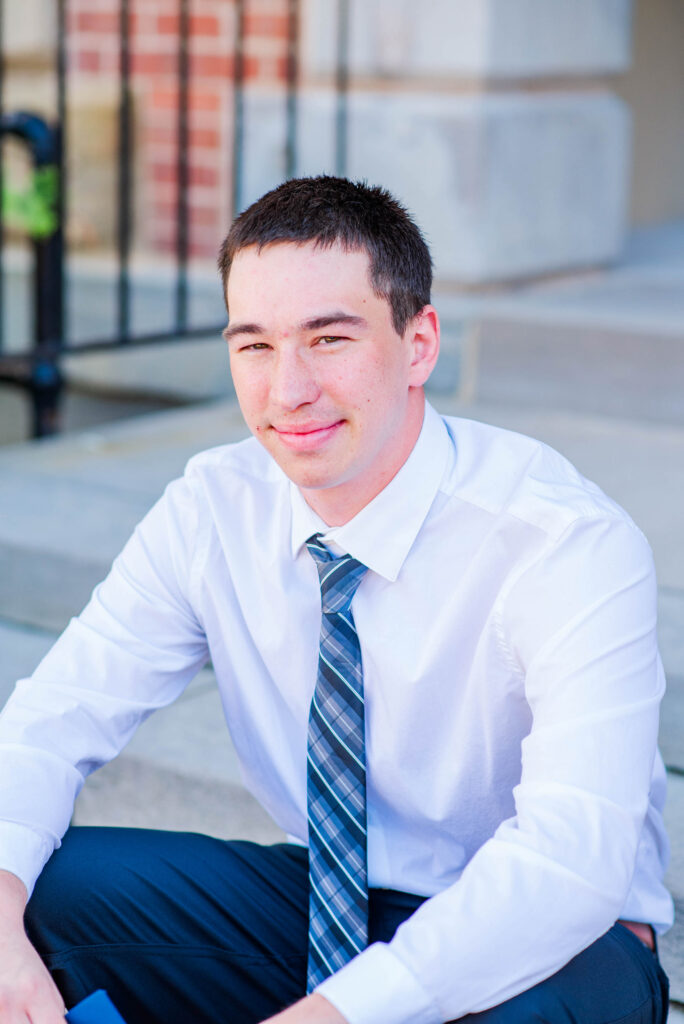 graduationphotoideasfor guys154 carrie white photography young man in a white dress shirt and striped tie sits on outdoor steps smiling at the camera