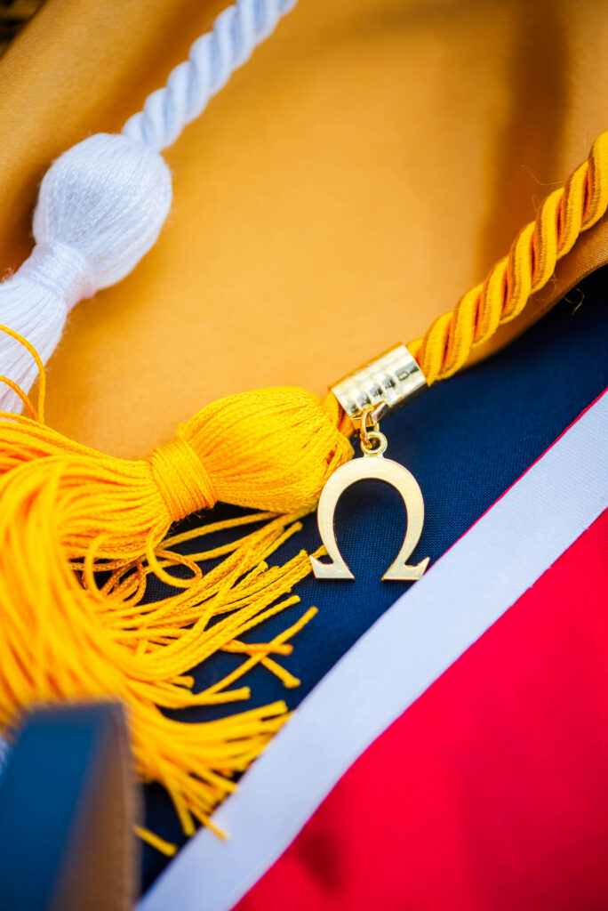 wvubaseballgradphotos14 carrie white photography close up of yellow graduation cords and a light blue tassel with a gold ring pendant on a red white and blue background