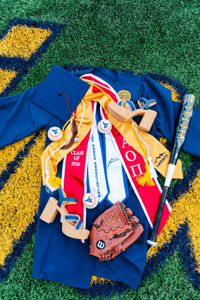 wvubaseballgradphotos16 carrie white photography graduates blue cap gown cords medals and a baseball glove laid on a field alongside a bat and shoes showing a celebratory senior theme