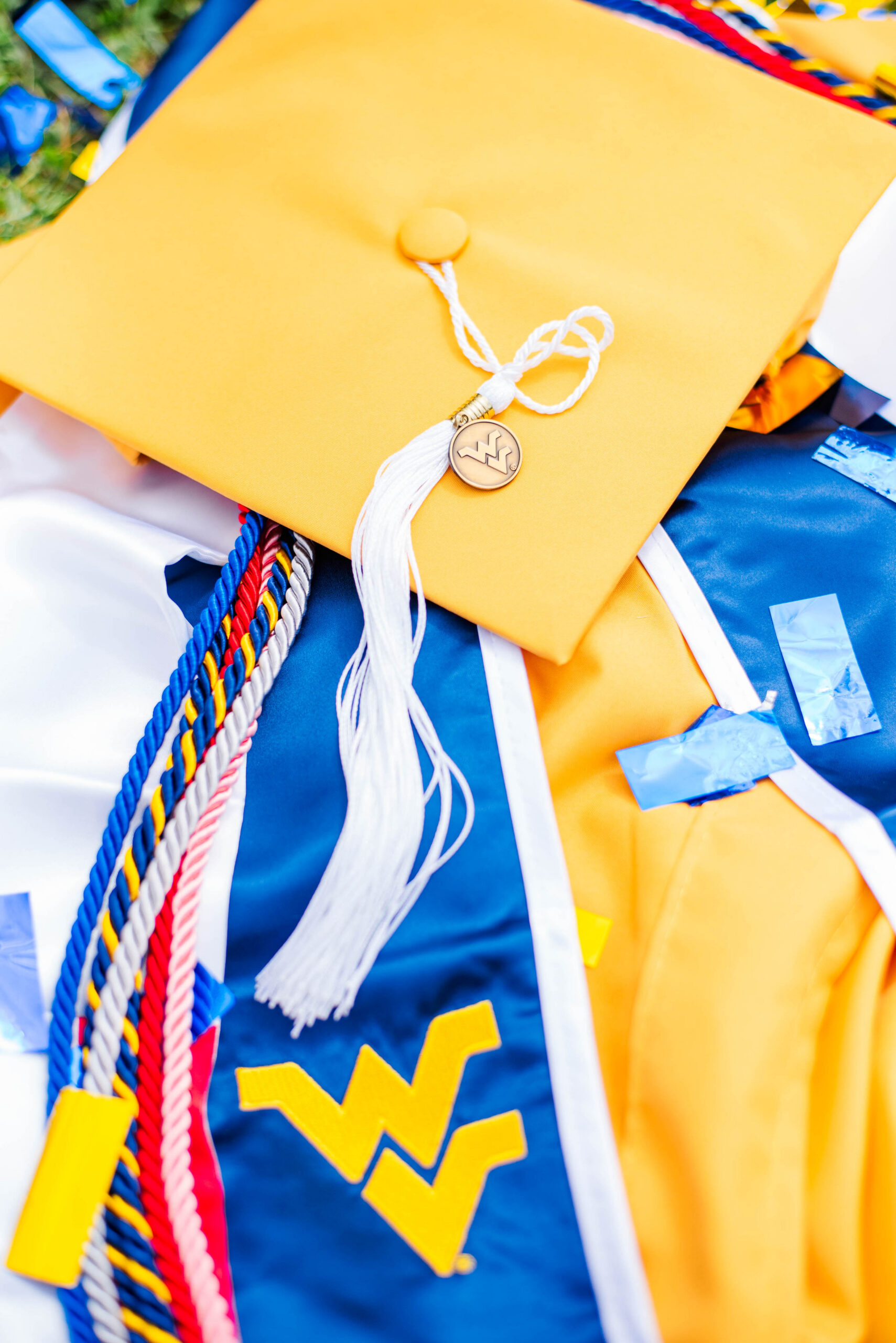close up of a yellow graduation cap with a white tassel resting on a blue gown and multicolored cords symbolizing graduation