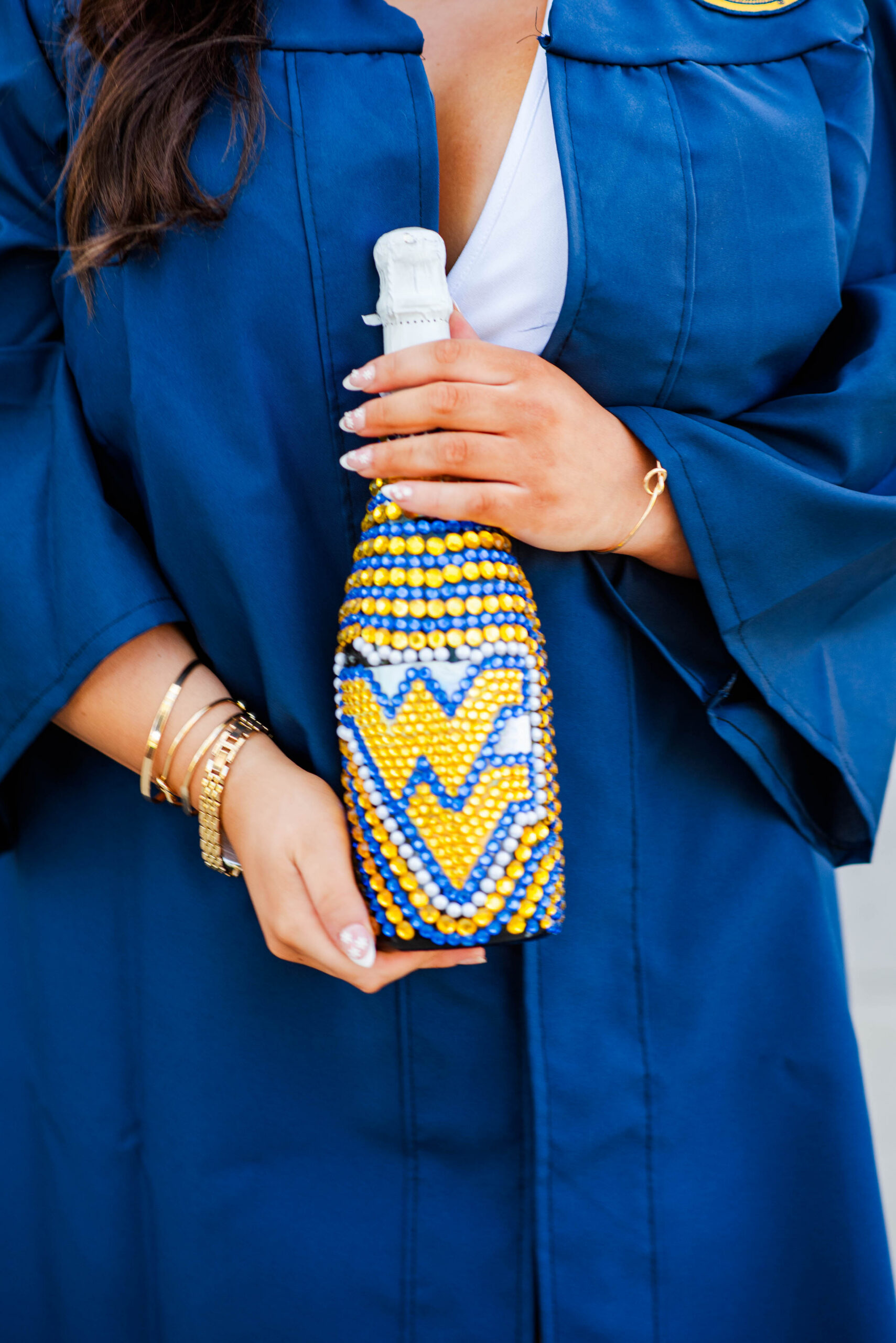 wvu spring grad photos with graduate in a blue gown holds a beaded decorative bottle with a white cap and blue yellow pattern