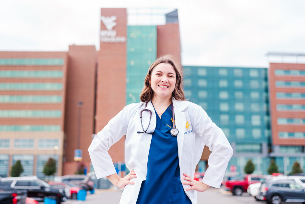 smiling female doctor in a white coat with a stethoscope outdoors in a hospital parking lot