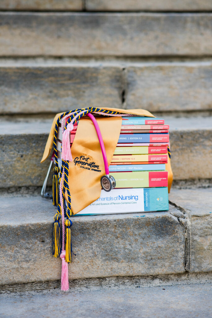stack of nursing textbooks on concrete steps with colorful graduation cords and a tan graduation bag draped over them