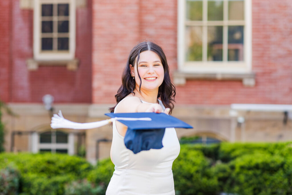 graduationcaptoss2 carrie white photography student wearing a white dress tossing graduation cap towards the camera and smiling